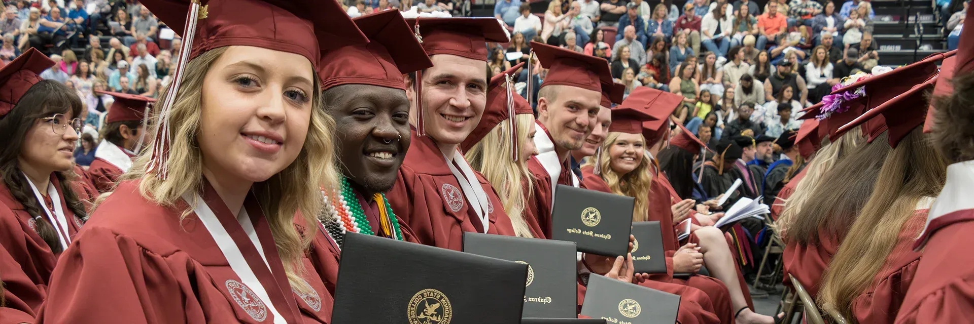 Group of college students at graduation smiling and showing their diplomas